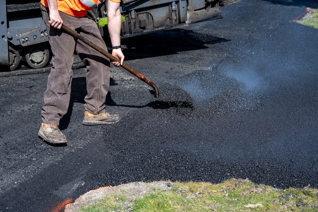 Worker shoveling hot mix asphalt for commercial pavement repair